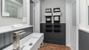 Un baño con lavamanos blanco, un espejo y dos toalleros con toallas.