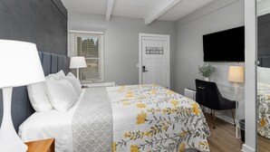 A hotel room with a bed, a desk, a chair, a TV, and a window with blinds.