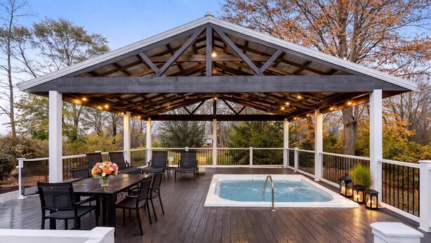 Una terraza techada al aire libre con jacuzzi, piso de madera y mobiliario exterior.