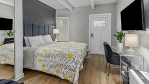 Una habitación de hotel moderna con una cama grande, un escritorio, una silla, un televisor y una puerta.
