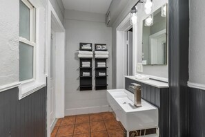 Une petite salle de bain avec un lavabo blanc, un miroir et des étagères où sont rangées les serviettes.