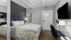 A modern hotel room with a large bed, a desk with a computer, a TV mounted on the wall, and a door with a window.