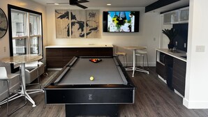 A modern living room with a pool table, a ceiling fan, and a TV mounted on the wall.