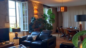 Een woonkamer met een leren bank, een eettafel, stoelen en een grote plant.