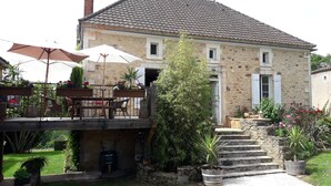 Een gebouw van natuursteen met pannendak, terras met parasols en een trap naar de ingang.