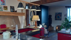 Een moderne keuken met een centraal eiland, rode kastjes, een ingebouwde oven en een hangende lamp.