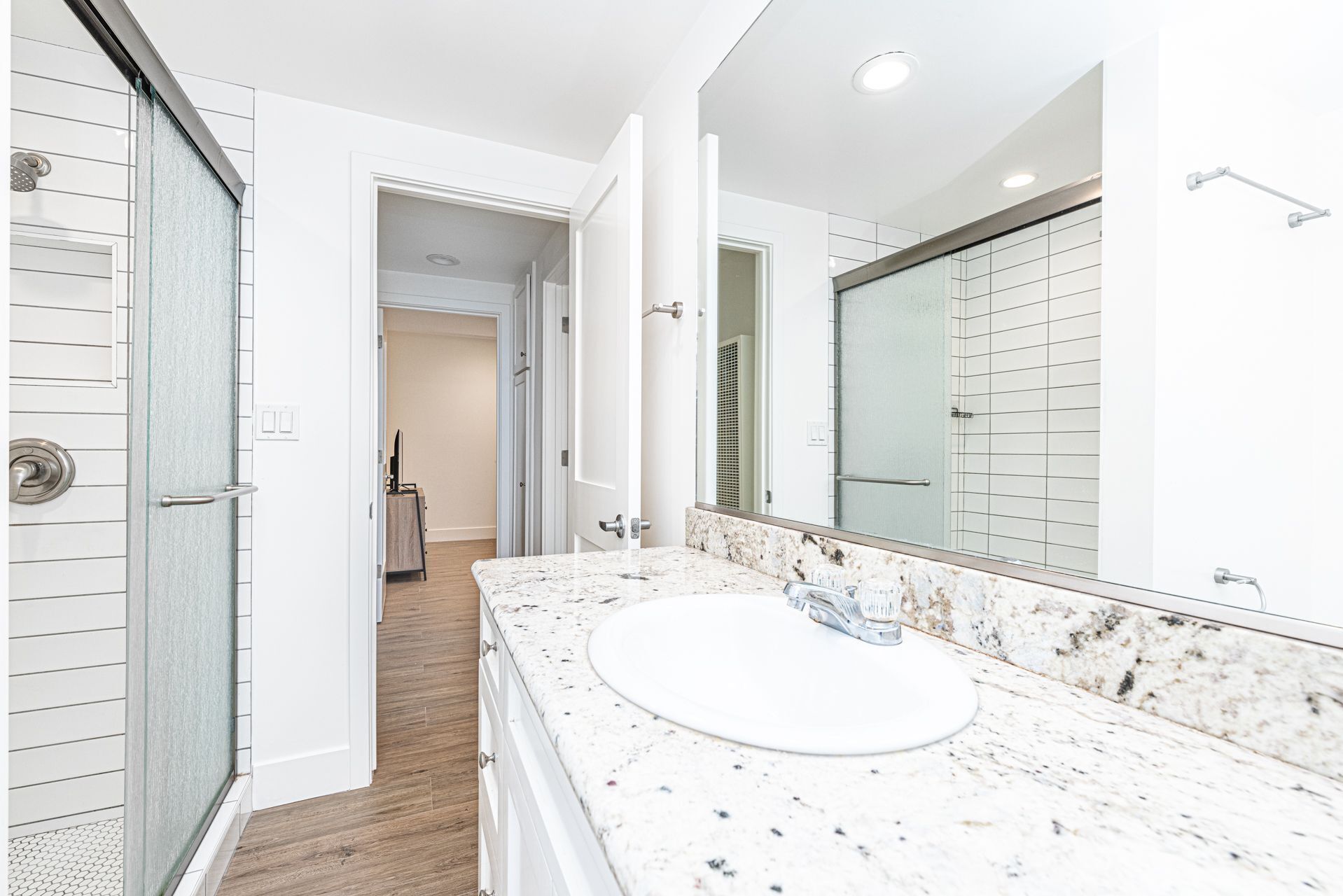Un baño moderno con cabina de ducha de vidrio, un lavamanos blanco con encimera de mármol y un espejo grande.