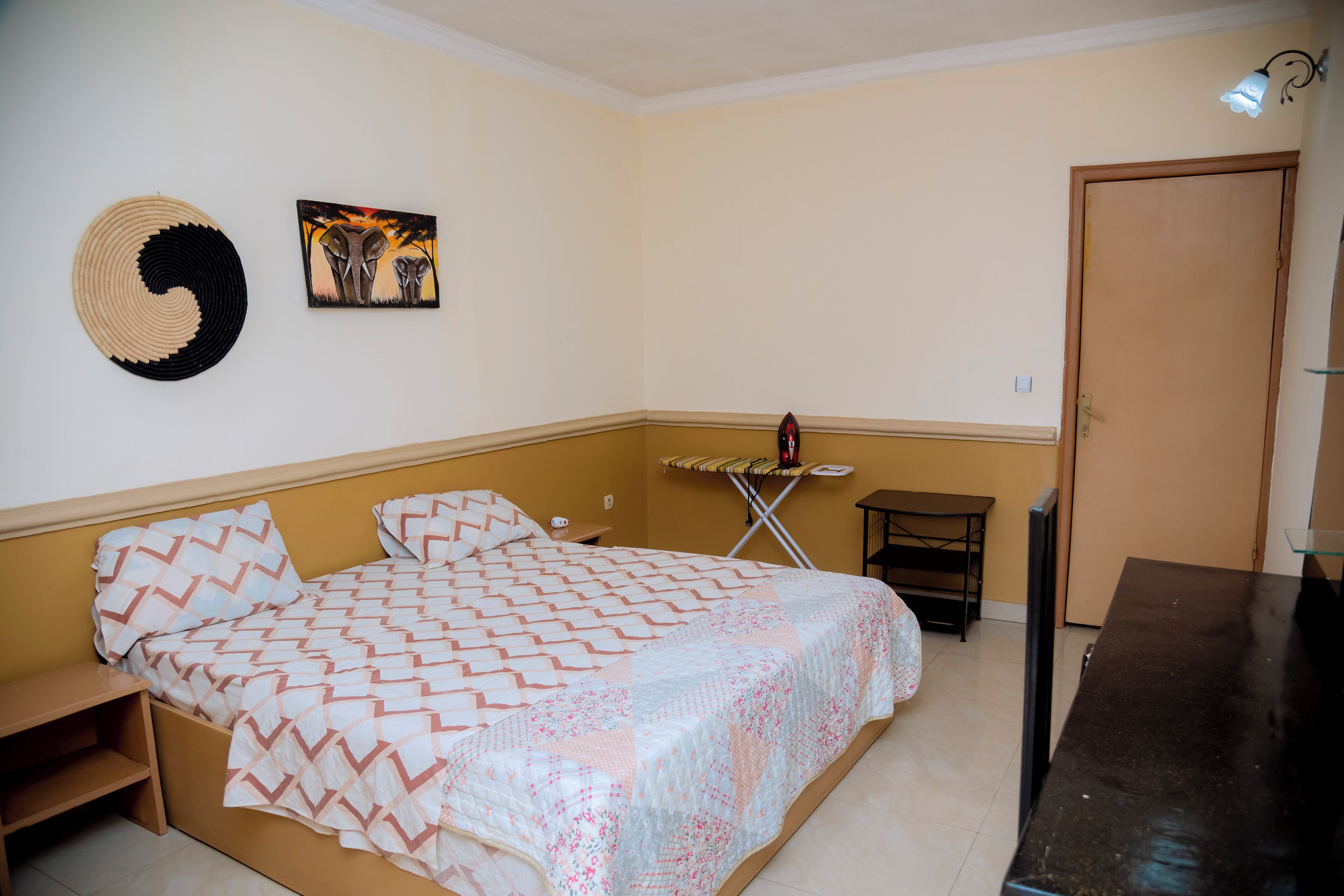 A bedroom with a bed, a wall hanging, a painting, a small table, and a door.