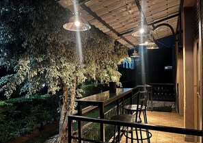 Un patio al aire libre con mesa y sillas de madera, rodeado de un jardín exuberante y una pérgola de madera.