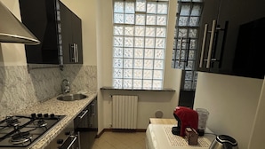A compact kitchen with a gas stove, a built-in oven, a refrigerator, and a window with patterned glass. - Chiossetto House apartment in downtown Milan (Milano)