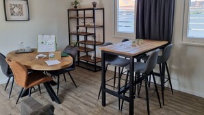 A dining area with a wooden table and chairs, a black metal shelving unit with plants, and a window with curtains. - 2B new vacation home with terrace and air conditioning (Westkapelle)