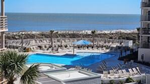 Zona de piscina con sillones de descanso y sombrillas, con vista a una playa y al océano.