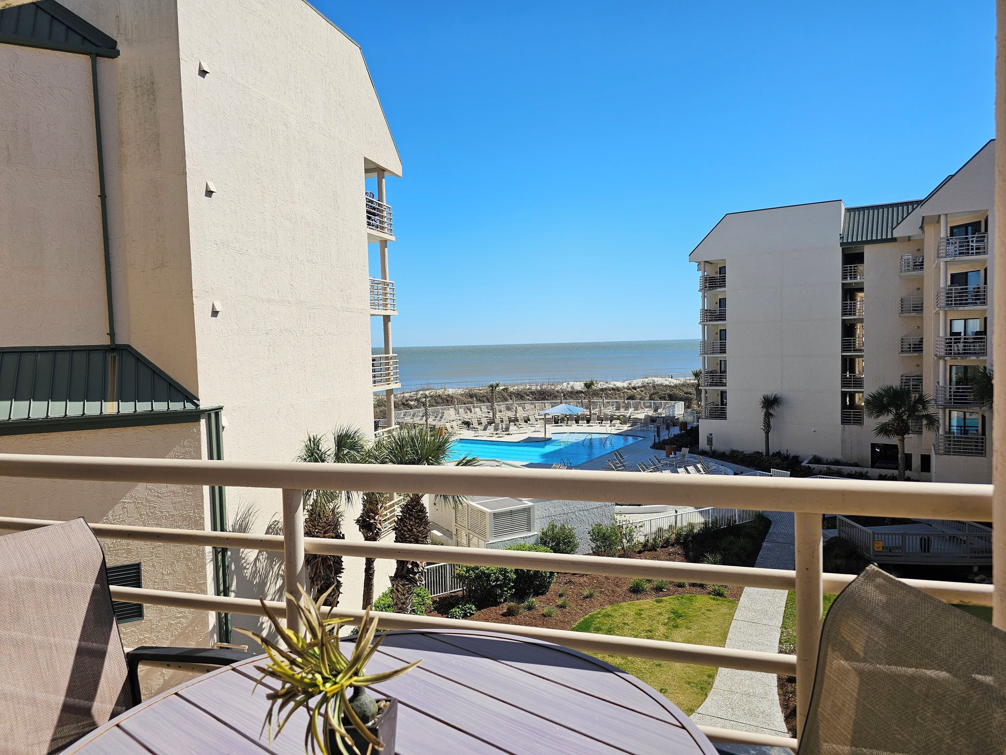 A balcony with a view of a swimming pool and beach, surrounded by buildings.