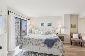 A bedroom with a bed, two bedside tables, a chair, and a view of a balcony with a building outside.