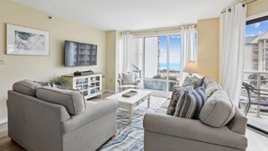 Sala de estar con dos sofás, una mesa de centro, un televisor y un mueble. Hay un ventanal con vistas a edificios y un balcón.