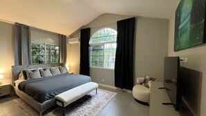Une chambre moderne avec un grand lit, un banc, une télévision et une fenêtre avec des rideaux.