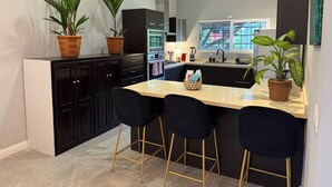 Une cuisine moderne avec des meubles de couleur sombre, un îlot central doté de tabourets et des plantes en pot.