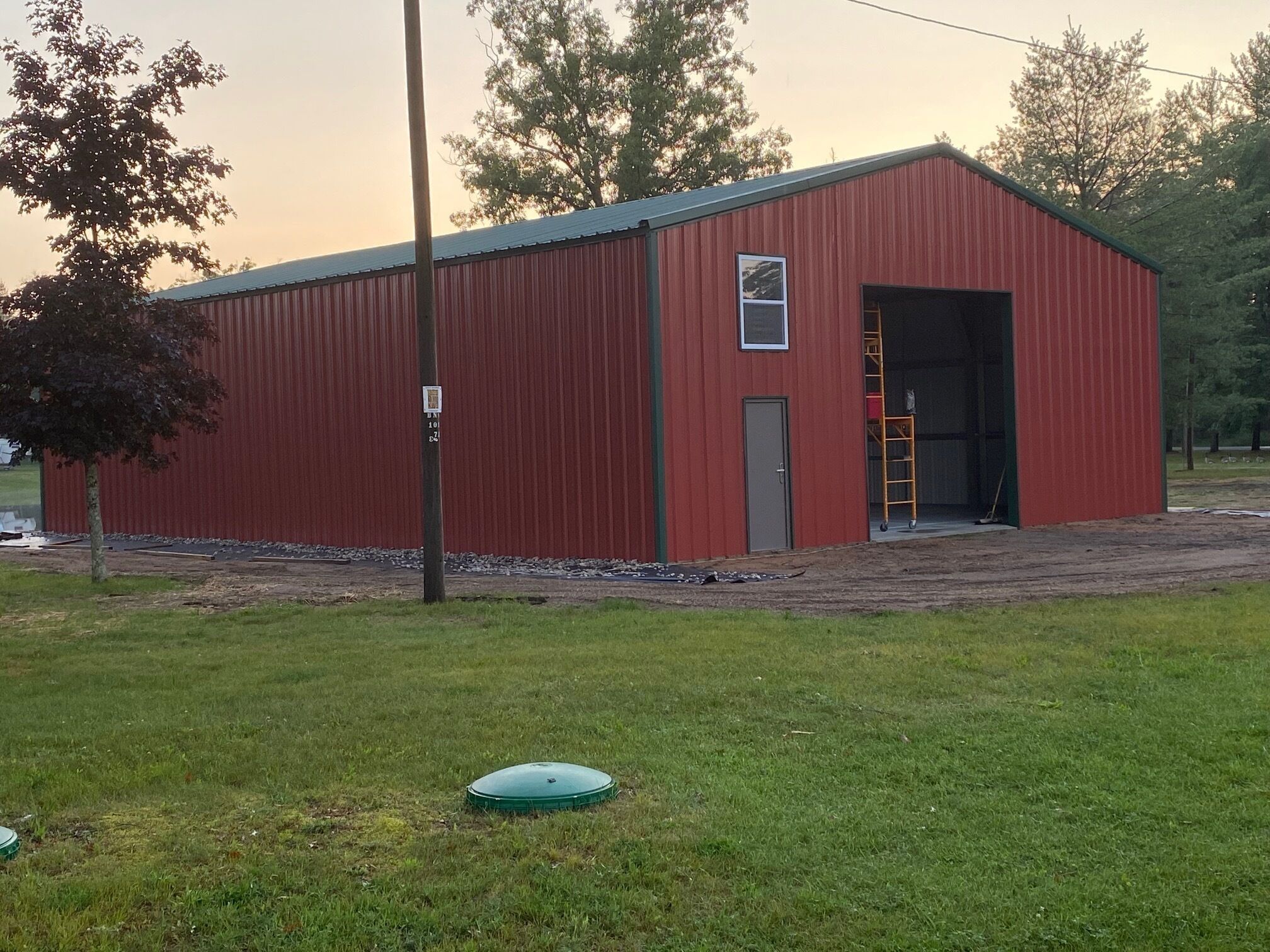 A red metal building with a door and a window, surrounded by grass and trees.