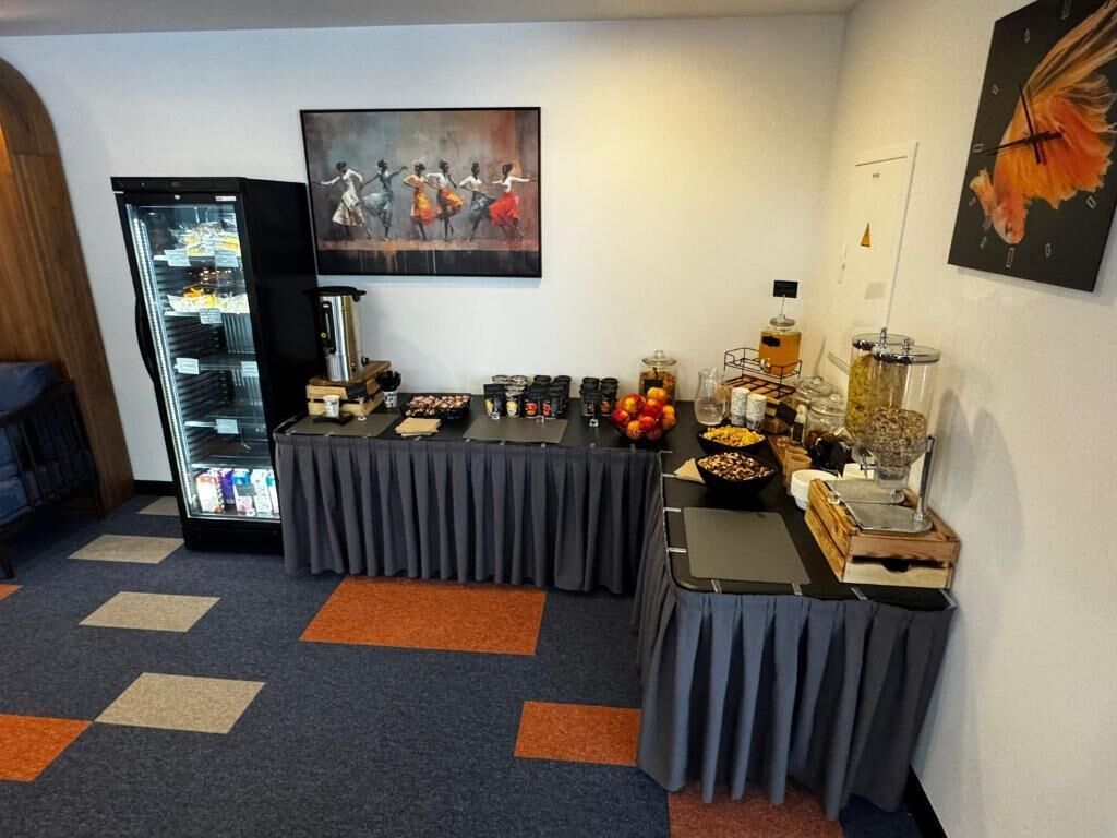 A buffet setup with a refrigerator, food containers, and a painting on the wall.