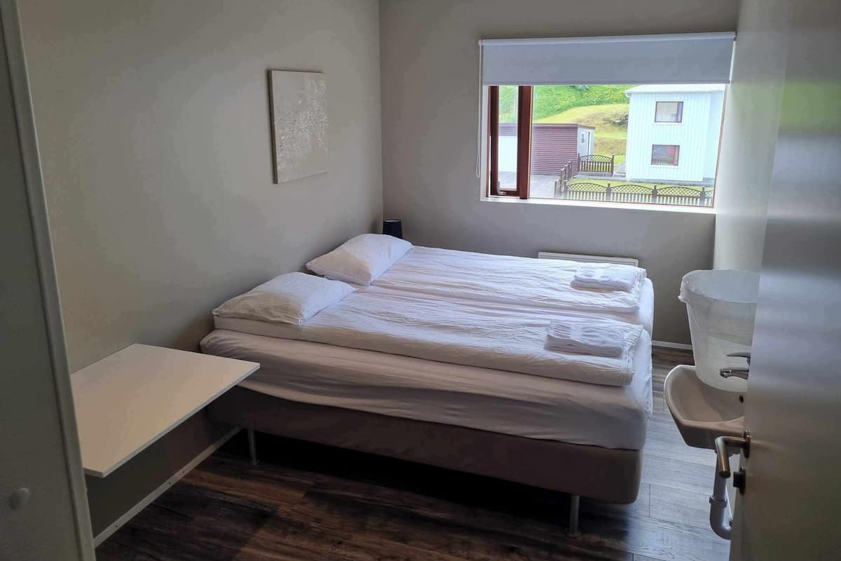 A small, modern hotel room with a single bed, a bedside table, a window with a view of the outside, and a toilet.