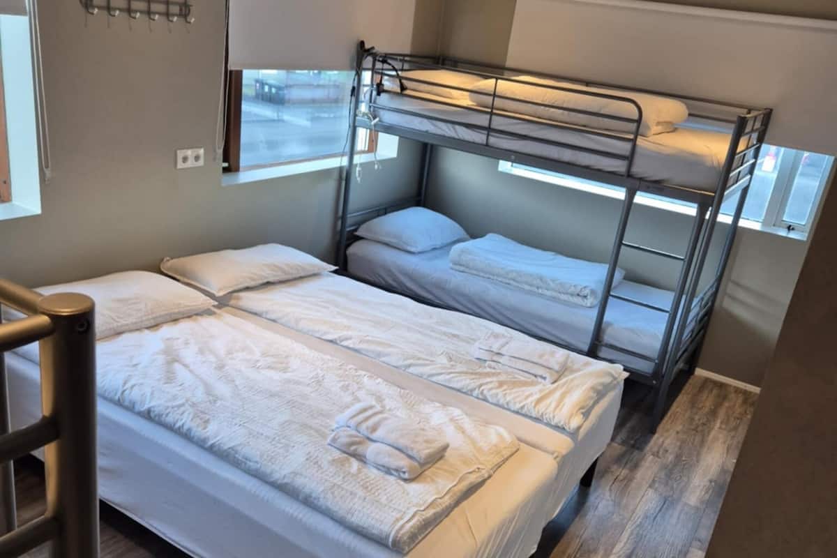 A bunk bed room with a wooden floor, a desk, and a window.