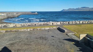 A coastal view with a rocky breakwater, a paved walkway, and a grassy area. - Vid hafid Guesthouse (Ólafsvík)