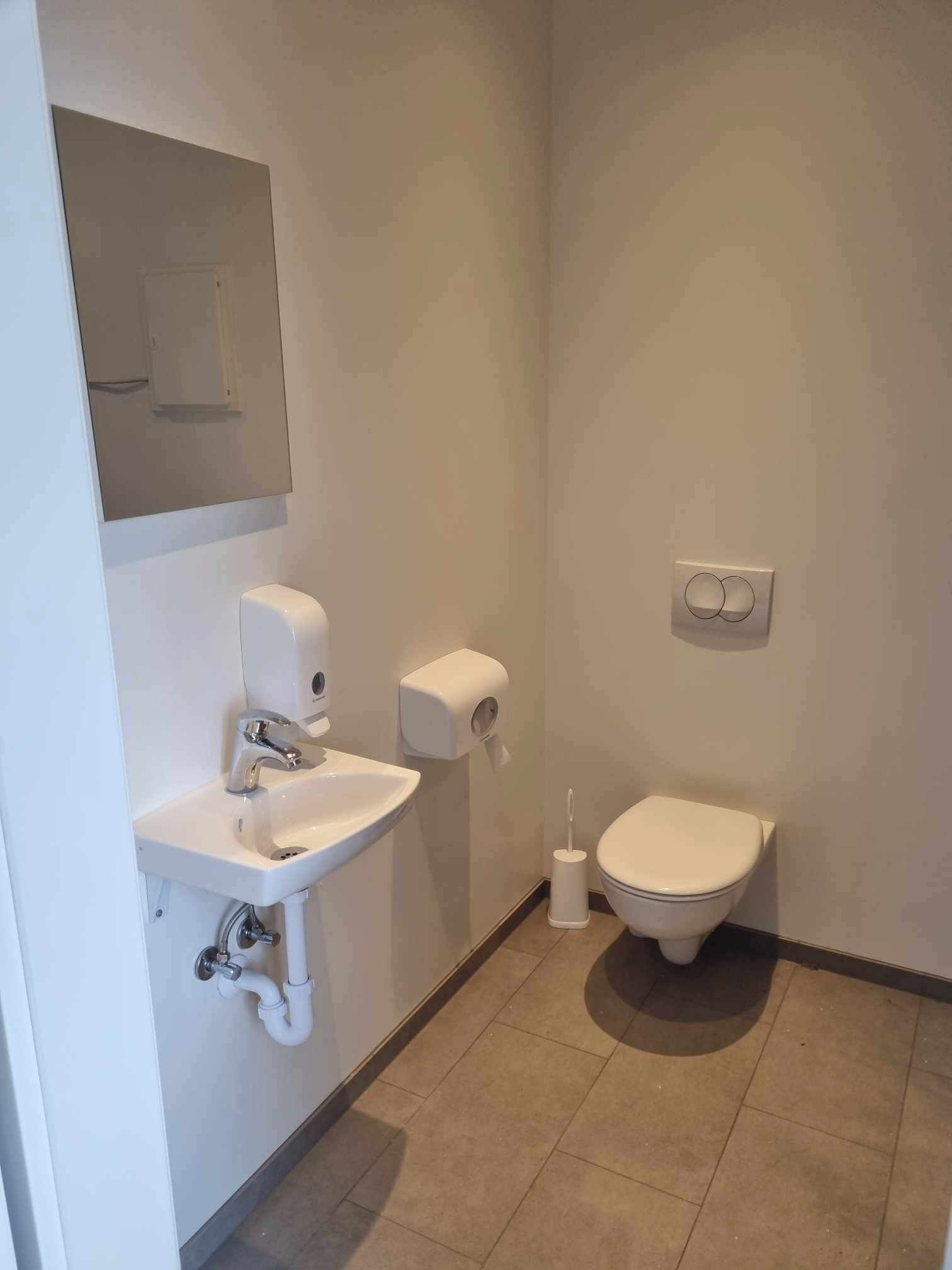 Un baño pequeño y limpio con lavamanos, inodoro y secamanos blancos.