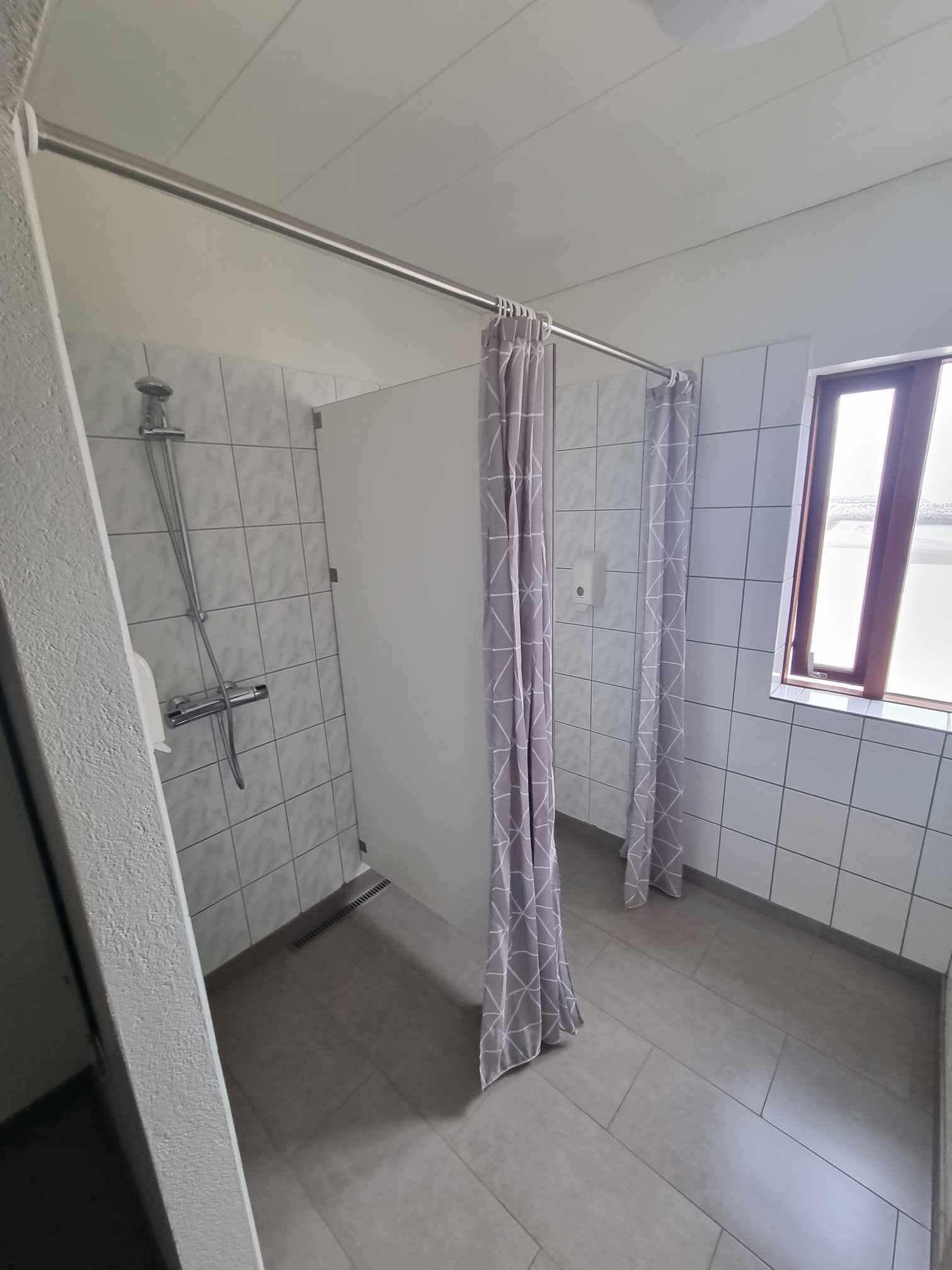 Un baño con ducha, paredes de azulejos y una ventana.