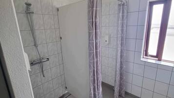 Un baño con ducha, paredes de azulejos y una ventana.