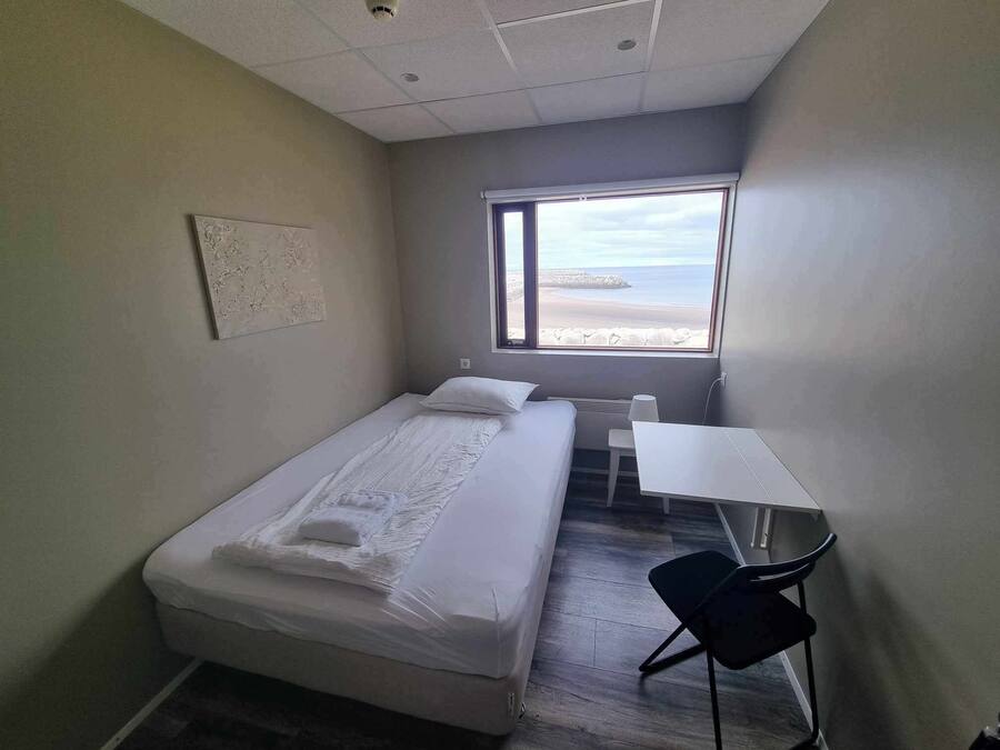 Una habitación pequeña y limpia con cama, escritorio y ventana con vistas a la playa.