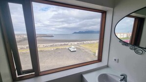 A bathroom with a large window offering a view of a beach and a car parked outside. - Vid hafid Guesthouse (Ólafsvík)