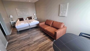 A modern hotel room with a double bed, a brown leather sofa, a dining table, and a small side table with a lamp. - Vid hafid Guesthouse (Ólafsvík)