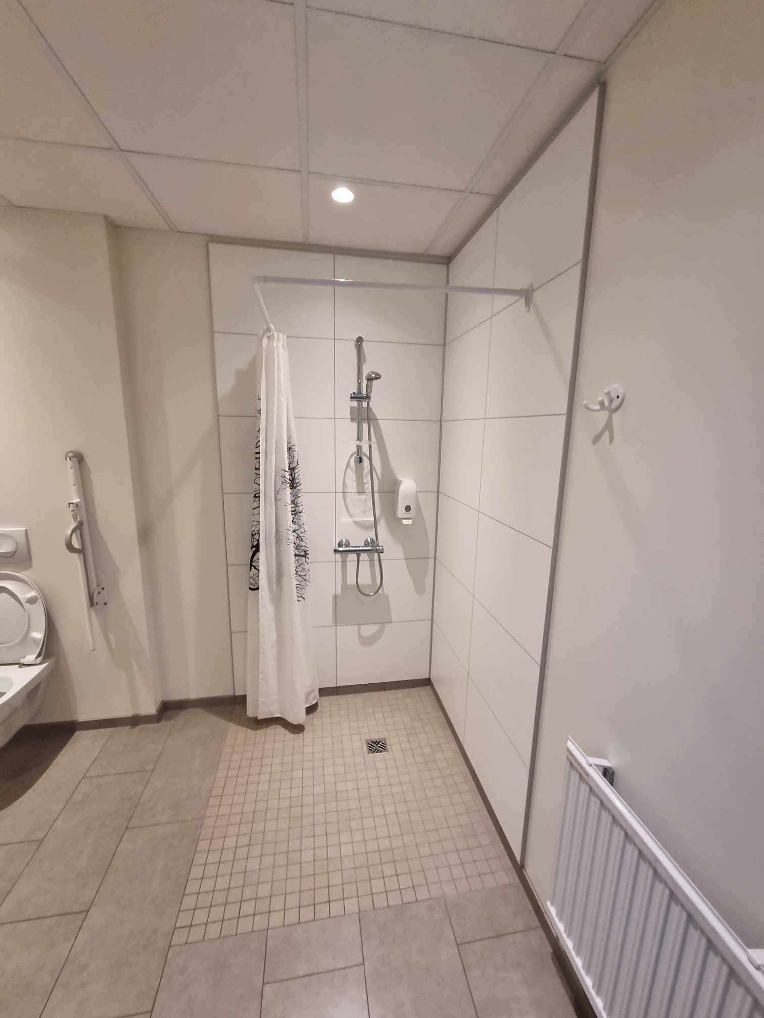A small, tiled bathroom with a shower, toilet, and a towel hanging on the wall.