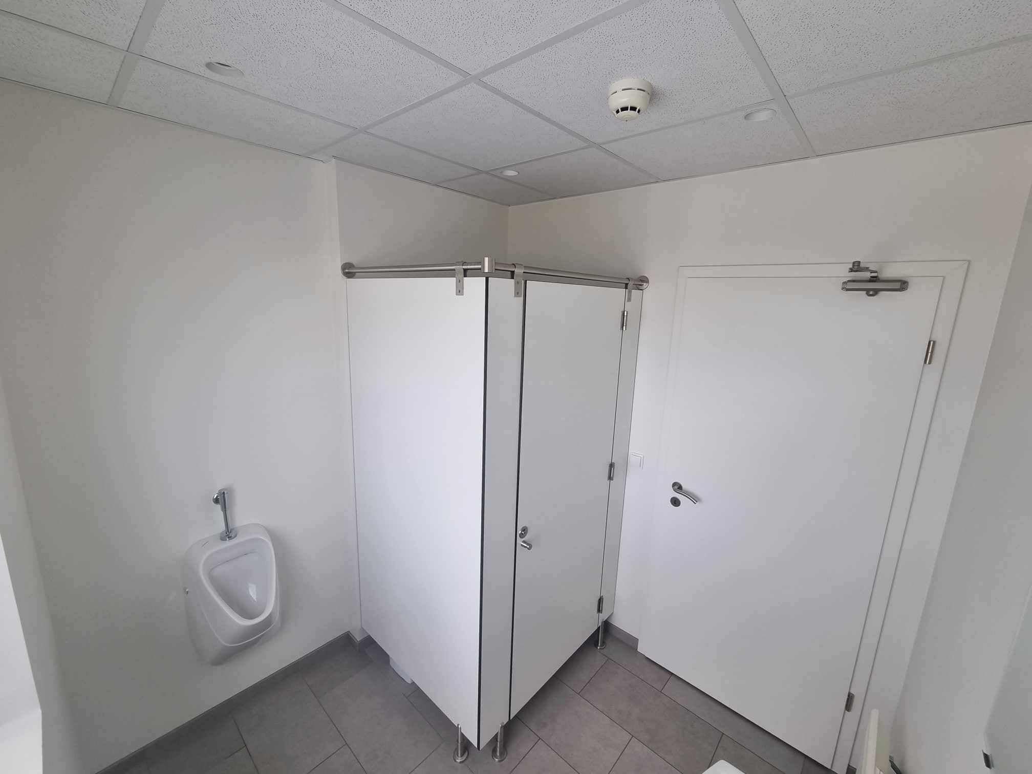 A restroom with two stalls, a urinal, and a door.