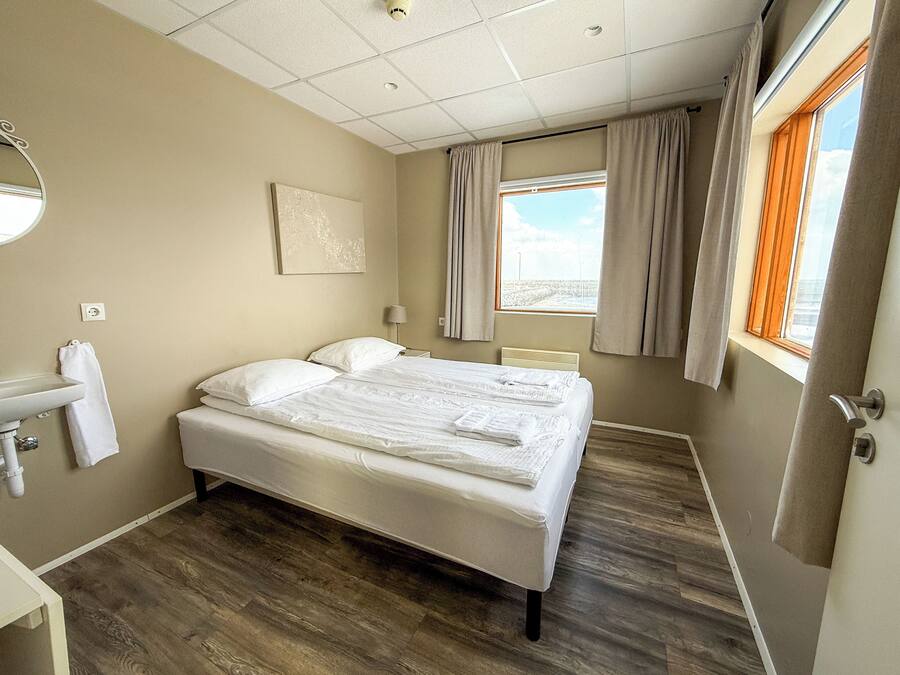 Una habitació d'hotel amb un llit, una tauleta de nit, una làmpada, una finestra amb cortines i una obra d'art penjada a la paret.