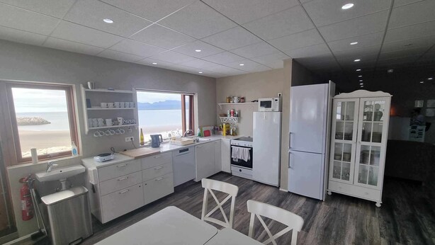 A modern kitchen with a view of the sea, equipped with a sink, stove, refrigerator, and a cabinet. - Vid hafid Guesthouse (Ólafsvík)