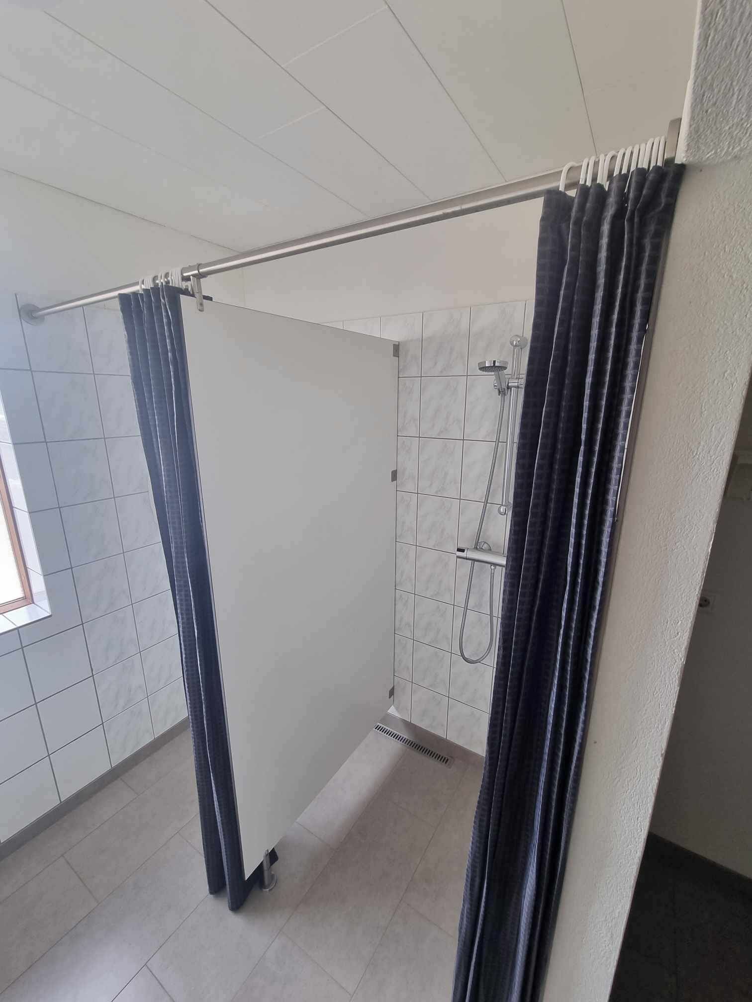Un baño con ducha, paredes de azulejos y ventana.