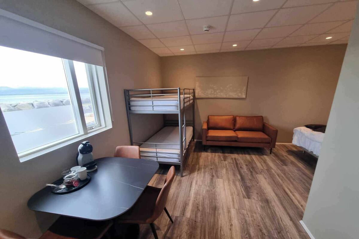A compact room with a bunk bed, a sofa, a dining table with chairs, and a window offering a view.