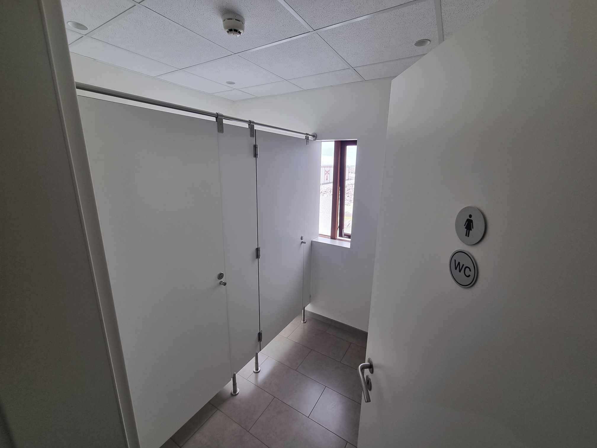 A hallway with a sliding door, a window, and a wall-mounted toilet sign.