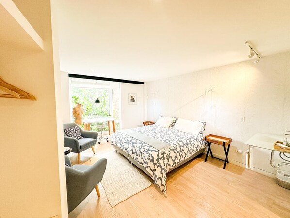 Un dormitorio moderno con una cama grande, un escritorio y una silla. Se ve un ventanal con vistas a zonas verdes.