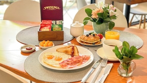 Une table mise pour le petit-déjeuner avec une boîte de thé Twinings, une assiette d’œufs, des toasts et un verre de jus d’orange.