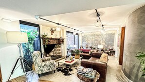 Un salon moderne avec une cheminée, des canapés en cuir, une table basse avec des livres et un lampadaire sur trépied.
