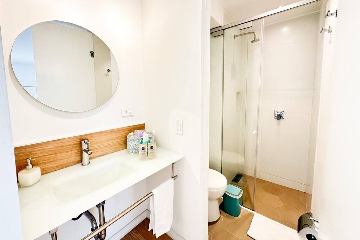 Een moderne badkamer met een ronde spiegel, een houten wastafelmeubel, een witte wasbak en een douche met glazen wanden.