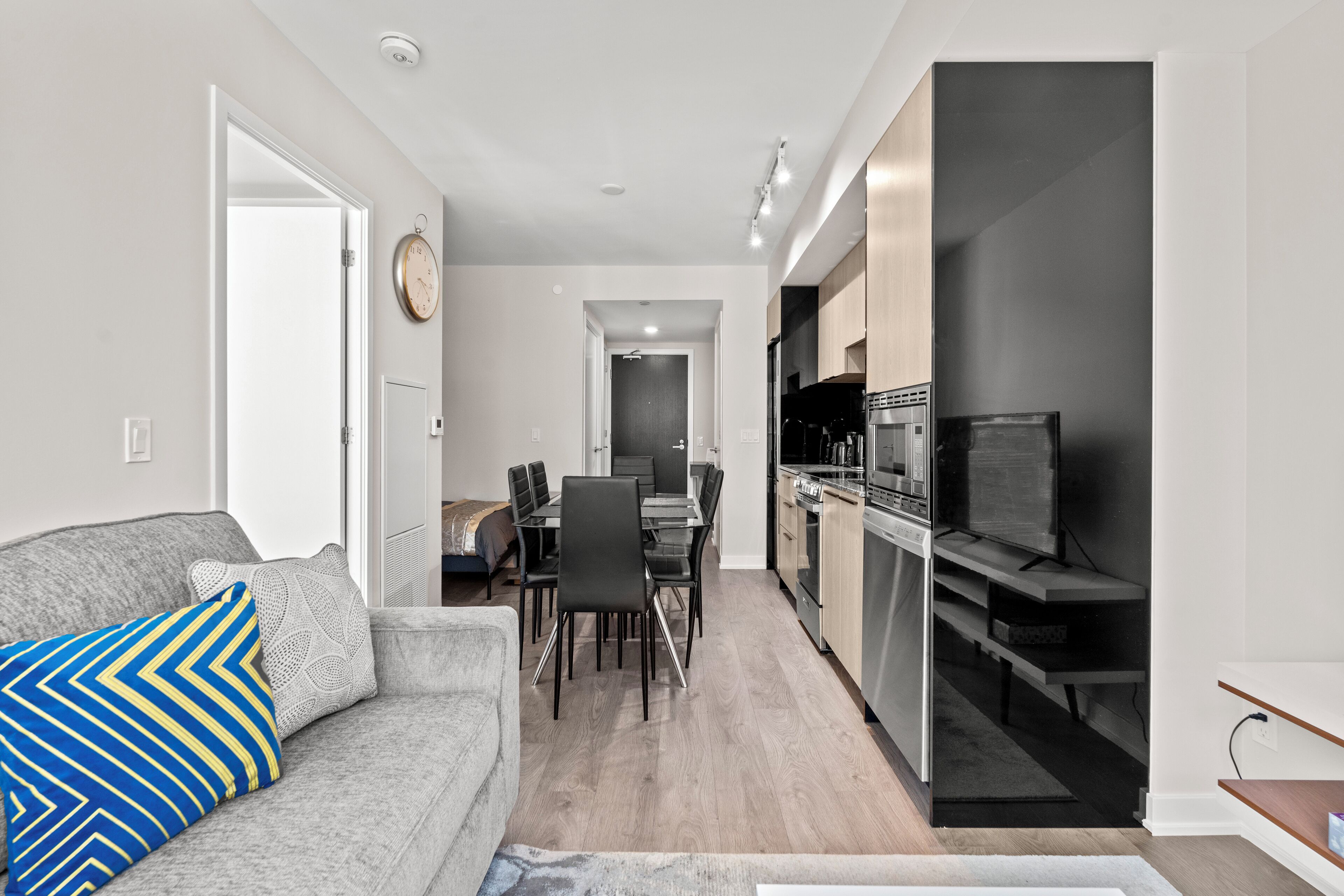 Una cocina moderna con horno y microondas integrados, un comedor con mesa y sillas, y una sala de estar con sofá y televisor.
