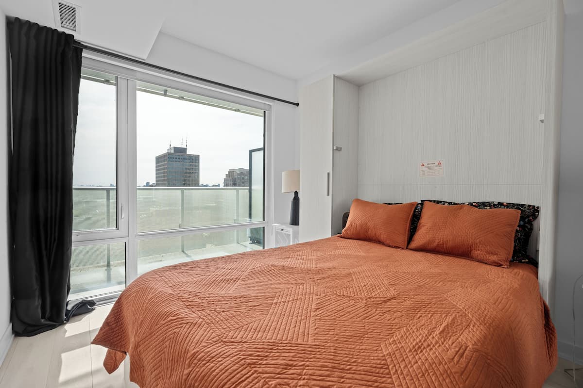 Una habitación de hotel con una cama grande, una ventana con cortinas, una lámpara y vistas a la ciudad.