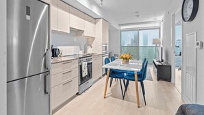 A modern kitchen with stainless steel appliances, a dining area with blue chairs, and a view of the city through large windows.