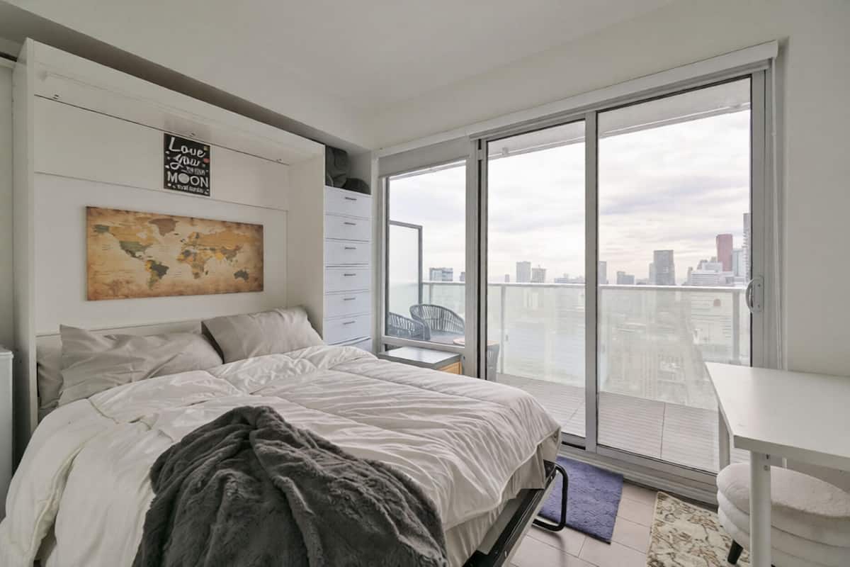 Un dormitorio moderno con una cama grande, un escritorio y vistas de la ciudad a través de un ventanal corredera.