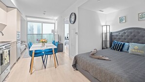 A modern hotel room with a dining area, a bed with a swan pillow, and a view of the city.