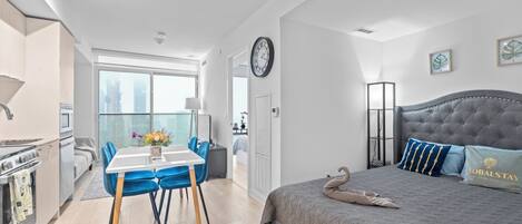 A modern hotel room with a dining area, a bed with a swan pillow, and a view of the city.