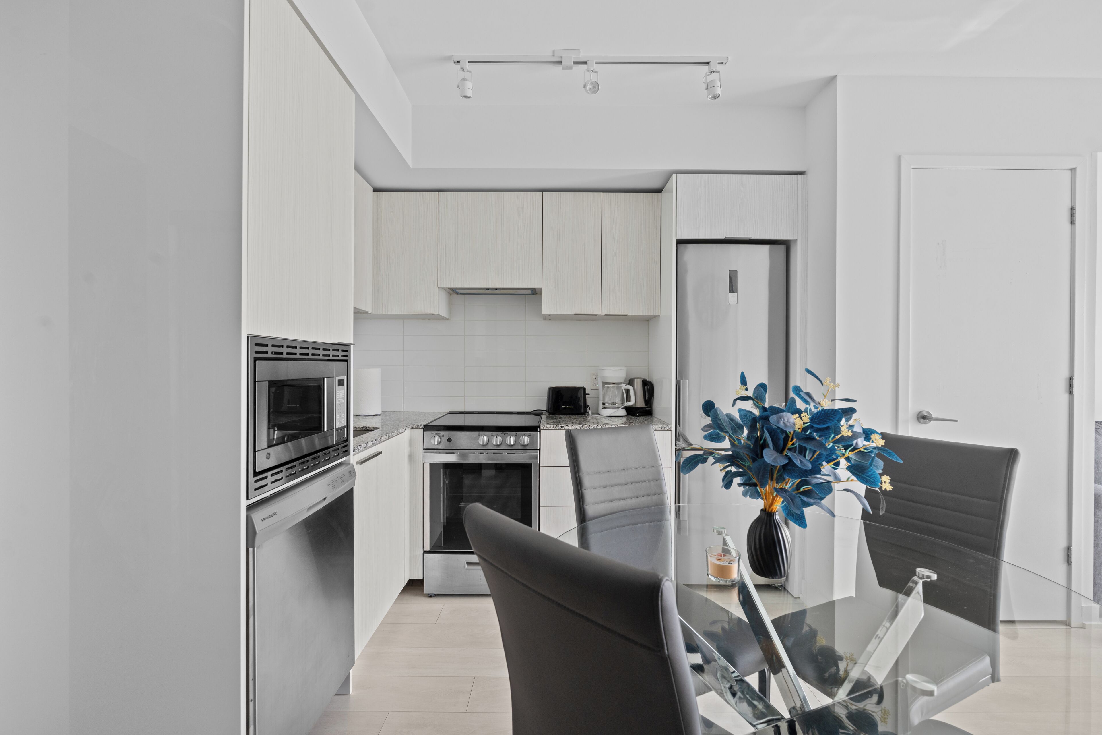 A modern kitchen with white cabinetry, a dining table with chairs, and a vase with flowers.